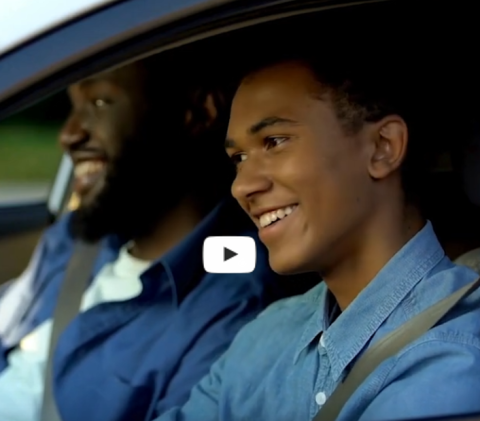 Teen boy and father sitting in car and smiling
